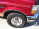 1994 Ford Bronco - Close-up view of the front fender and wheel of a red 1994 Ford Bronco, chrome accents and Bridgestone tires.
