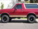 1994 Ford Bronco - Side profile of a red Ford Bronco with tan accents and lifted suspension.