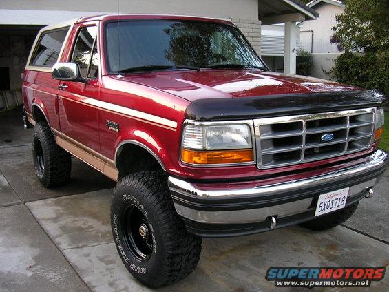 Red Ford Bronco with tan top, lifted suspension, and chrome grille. License plate 5XQS718