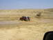 1994 Ford Bronco - A red and white SUV navigates through a muddy terrain under a clear blue sky.