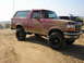 1994 Ford Bronco - This muddy 1994 Ford Bronco is seen off-road, with a dirt bike and another vehicle in the background.