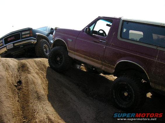 Maroon 1994 Ford Bronco and GMC truck on dirt hill