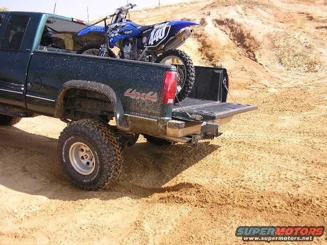 Pickup truck with a dirt bike in the bed, parked on a dirt lot