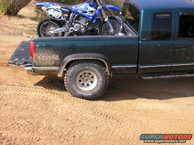 Dark green pickup truck side view with a blue dirt bike in the bed