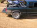 1994 Ford Bronco - A dark green pickup truck carries a blue dirt bike in its bed, parked on a dirt surface.