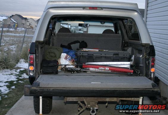 Silver Ford Bronco rear cargo area loaded with gear, including a toolbox and sleeping bag. The tailgate is open