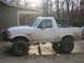 1996 Ford Bronco - A muddy 1996 Ford Bronco with a roll cage and large off-road tires is parked outside a building.