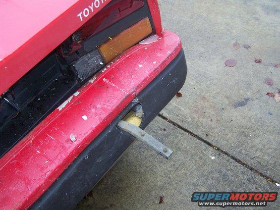 Red Toyota car rear bumper with black trim, showing damage and a metal bracket protruding