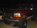 1992 Ford Bronco - This red Ford Bronco is parked next to another vehicle at night.