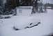1996 Ford Bronco - A vehicle is completely covered in snow, with a small white shed and trees in the background.