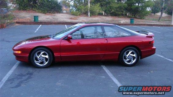 Red coupe parked in a lot, side view. Chrome wheels, spoiler, tinted windows
