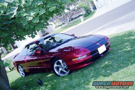 Red and black 1996 Ford Probe parked on grass, 3/4 front view