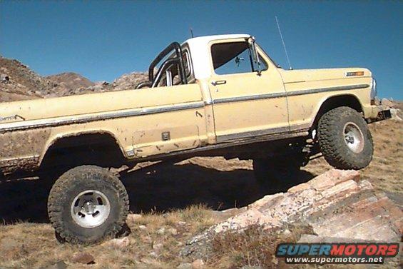 Yellow Ford F-Series pickup truck with roll bar, lifted suspension, and off-road tires climbing rocks