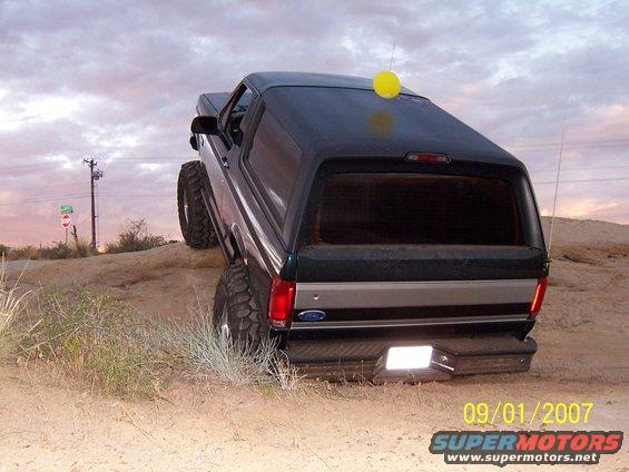 Ford Bronco climbing dirt hill, yellow ball on roof