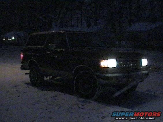 1990 Ford Bronco parked in snow at night, headlights on