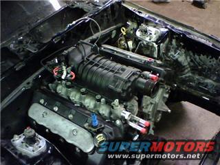 Engine bay with supercharger and V8 engine, Supermotors.net logo visible