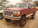 1992 Ford Bronco - A lifted maroon 1992 Ford Bronco with a white top is parked outside on a wet day.