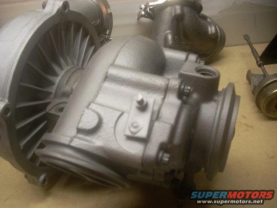 Close-up of turbocharger components, one with visible fins. Another part with a rod is to the right