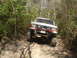 1989 Ford Bronco - White off-road SUV navigates a wooded trail with large tires and a modified front bumper.