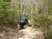 1989 Ford Bronco - A blue Jeep Wrangler navigates a steep, wooded trail with large off-road tires.