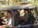 1989 Ford Bronco - Two people are inside a dark blue Jeep with a soft top, driving on a wooded trail.