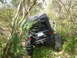 1989 Ford Bronco - A black Jeep Wrangler is seen tilted off-road, with its rear bumper and Florida license plate visible amidst foliage.