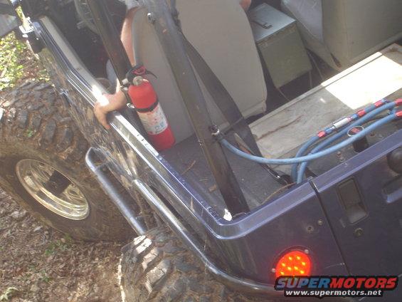 Side view of a dark blue Jeep interior. Fire extinguisher mounted on the side. Some blue hoses and a metal box are visible in the back