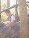 1989 Ford Bronco - Man drives a muddy off-road vehicle off-road, navigating around a tree.