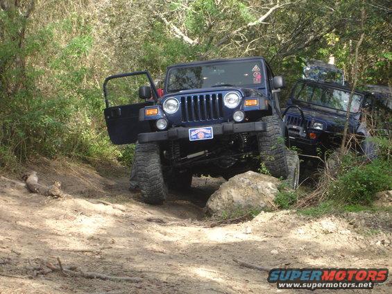 Blue Jeep Wrangler with open driver's door on rocky terrain