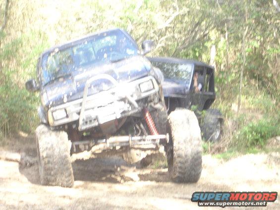 Two off-road vehicles with large tires in mud, one with a bull bar