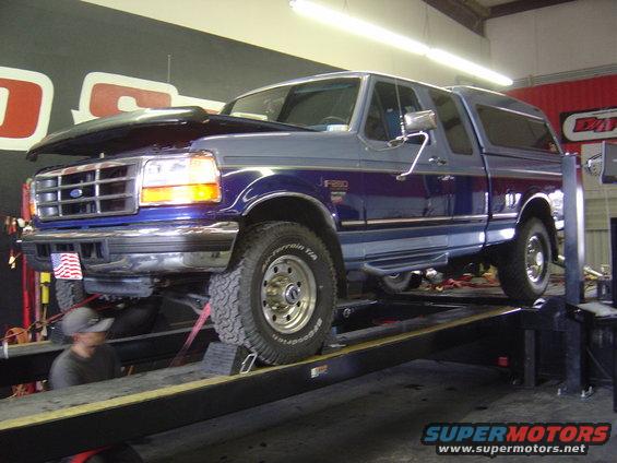 Blue and gray Ford F-250 pickup on a lift, hood up. F-250 badge visible