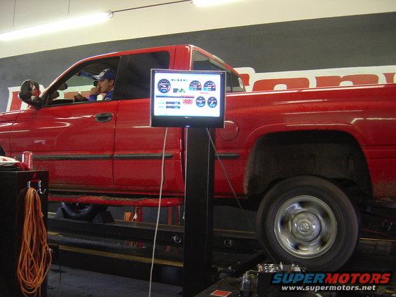Red pickup truck on a dynamometer, side view. The truck has a crew cab and a long bed