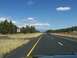 1995 Ford C-350 (Centurion Conversions) - A highway stretches through a landscape of trees and distant mountains under a blue sky with scattered clouds.