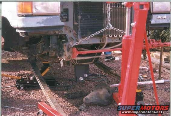 Truck front suspension being worked on, with a red engine hoist and jack stands