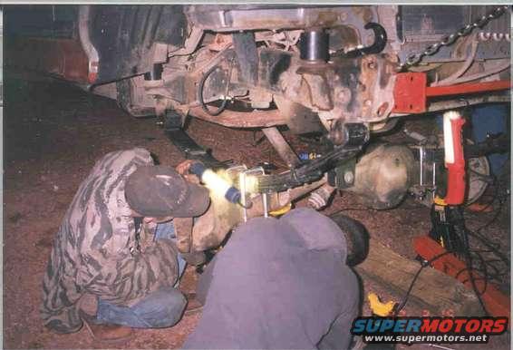 People working on the rear leaf springs and axle of a truck