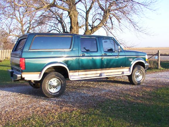 Green SUV with tan trim, side view, parked on gravel with grass and trees