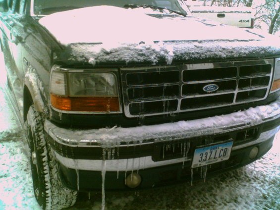 Front of a dark-colored Ford truck covered in snow and icicles. License plate reads 337LCB