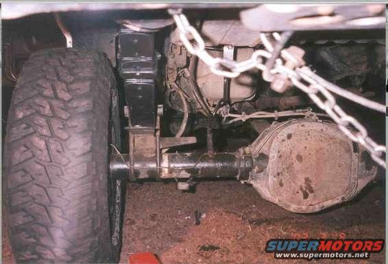 Close-up of a vehicle's rear axle, differential housing, and suspension components, including a large tire and chains
