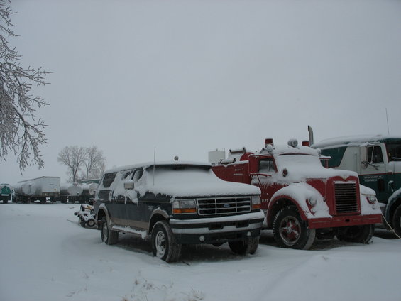 1995 Ford Bronco parked next to a red fire truck and a green truck in the snow