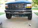1995 Ford C-350 (Centurion Conversions) - Front view of a Ford truck, focusing on the bumper and grille. Some small parts are scattered on the concrete below.