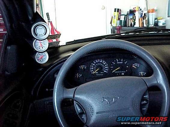 Interior shot of a 1994 Ford Mustang GT with a steering wheel, dashboard gauges, and aftermarket gauges on the pillar