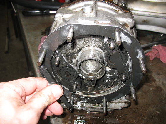 Close-up of a greasy, disassembled vehicle transmission component with a hand holding a metal plate