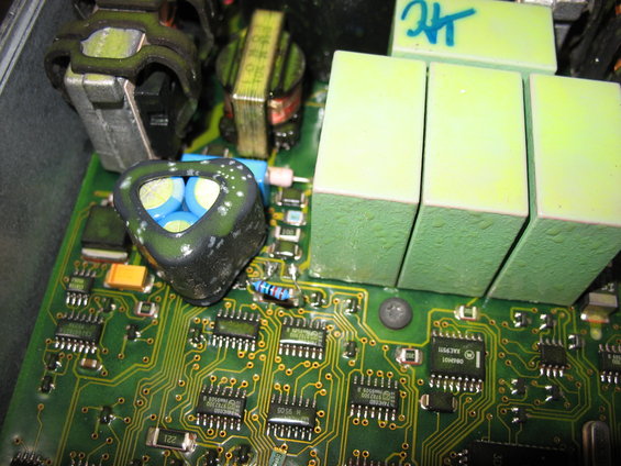 Close-up of an electronic control unit with green relays and a triangular capacitor