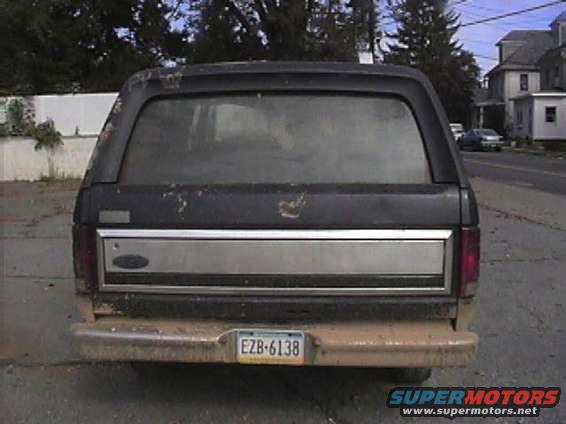 Rear view of a dark-colored Ford Bronco with a silver trim panel and a license plate reading EZB-6138