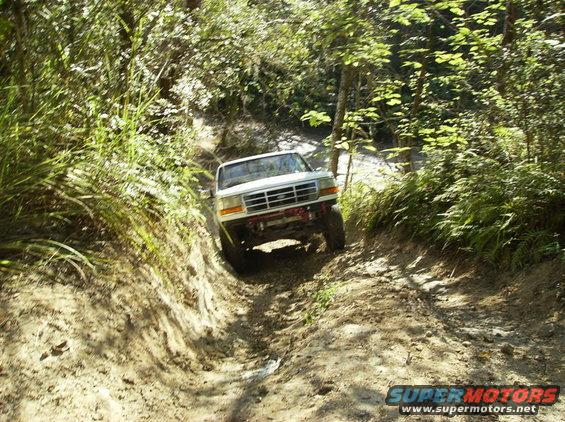 White Ford Bronco driving off-road on a muddy trail, front 3/4 view