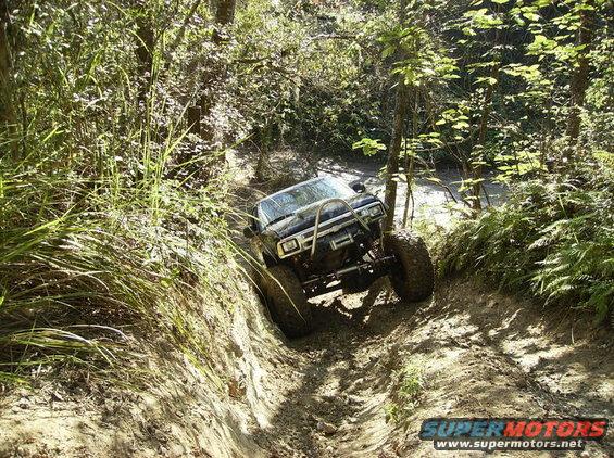 Off-road vehicle with large tires driving down a steep, muddy trail surrounded by trees and foliage