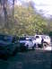 1989 Ford Bronco - Several SUVs are parked on a dirt lot surrounded by trees, with one person standing near the rear of a white SUV.