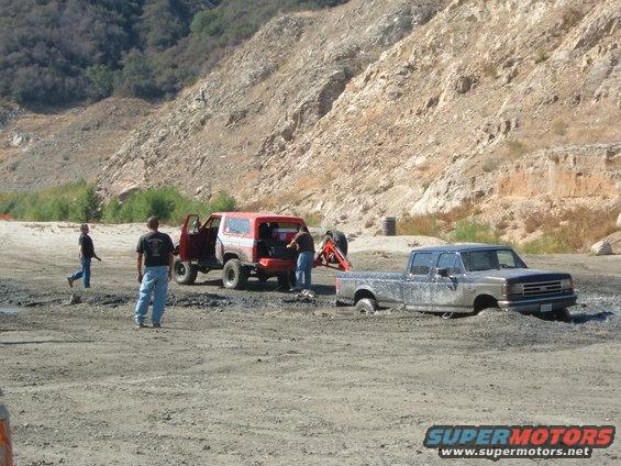 Red 1981 Ford Bronco and stuck pickup truck in mud