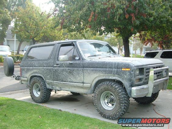 Mud-covered Ford Bronco with spare tire on back, parked on driveway