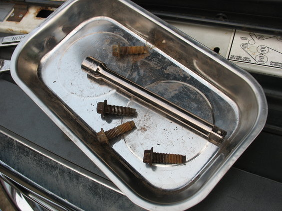 bolts and socket extension in a metal tray, sitting on a car engine part